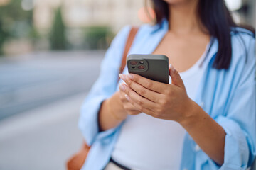 Close up of female hands holding a modern smartphone, browsing the internet and engaging with social media on a bustling city street