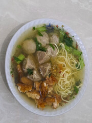 Bowl of traditional indonesian meatball noodle soup with vegetables served on white plate for asian cuisine