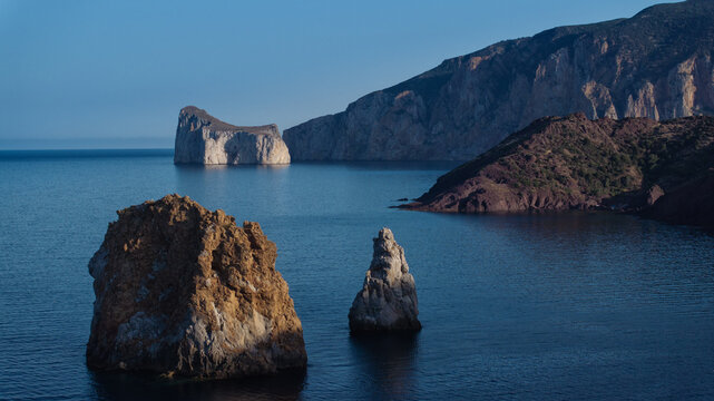 Aerial view of the rugged coastline meets the tranquil blue sea, with Pan di Zucchero standing majestically in the distance, Sardinia, Italy.