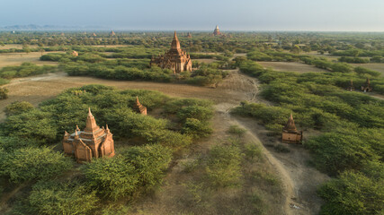 Aerial view of ancient temples rising from the verdant landscape, their weathered brick facades glowing softly in the diffused light, Old Bagan, Mandalay Region, Myanmar.