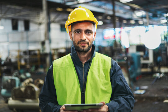 man wearing yellow hard hat and green vest is holding tablet