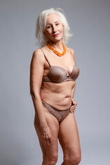 Natural Portrait of Mature Blond Caucasian Woman in Brown Lingerie Wearing Amber Necklace Posing Over Dark White Background