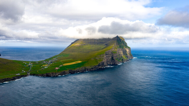 Aerial view of a dramatic coastal landscape where the emerald slopes of Kaap Enniberg meet the azure embrace of the sea, crowned by ethereal clouds, Vi&Atilde;&deg;arei&Atilde;&deg;i, Vi&Atilde;&deg;oy, Faroe Islands.