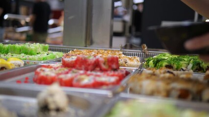 A womans hand picks sushi at a Chinese restaurants all-you-can-eat buffet. Conveys abundance and diverse culinary options.