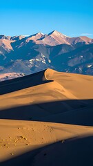 Sand dunes and snow-capped mountains under a vibrant blue sky.