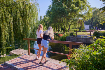 Two middle-aged sisters spending a summer morning in the park by a lake relaxing and having fun.