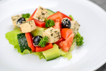 Greek salad with olives in a white plate on a gray background macro photo