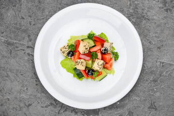 Greek salad with olives in a white plate on a gray background