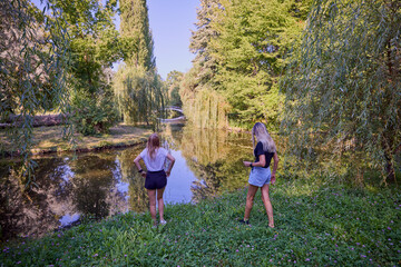 Fototapeta premium Two middle-aged sisters spending a summer morning in the park by a lake relaxing and having fun.