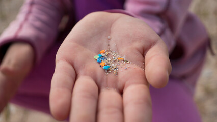 Child's hand on a beach, a symbol of the future generation inheriting a world with microplastic pollution. Generational plastic waste concept.