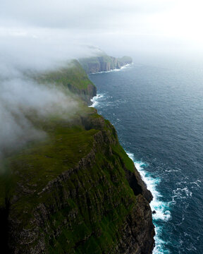 Aerial view of dramatic cliffs plunge into the turbulent sea, shrouded in ethereal mist near Dunnesdrangar, S&Atilde;&cedil;rv&Atilde;&iexcl;gur, V&Atilde;&iexcl;gar, Faroe Islands.