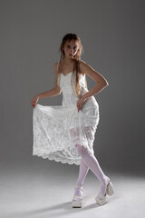 Naklejka premium Young woman poses elegantly in a white lace dress, showcasing a unique style with graceful expression and modern footwear in studio