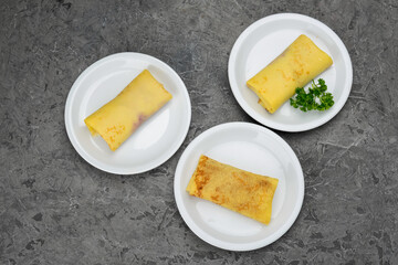 three pancakes with filling in three white plates on a gray background