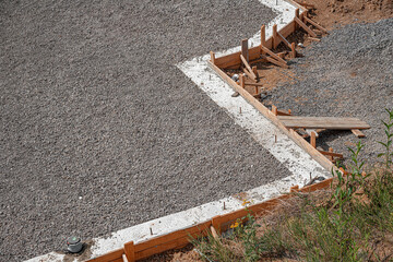 A newly poured concrete slab foundation and pathway, framed by wooden formwork and surrounded by loose gravel and brown soil on a sunny construction site.