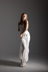 Fototapeta premium Model poses in elegant white dress on a plain background during a fashion photoshoot at sunset