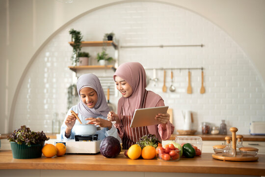 Happy Muslim mother and her daughter using digital tablet preparing a meal in Kitchen