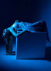 Model posed dramatically on a block in blue lighting during a creative indoor photoshoot in an...