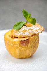 Whole baked apple dessert in a white plate on a gray concrete background close-up