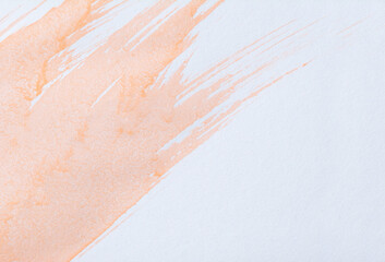 Light orange watercolor wash and splatters on textured white paper. Paint forms several elongated fluid streaks that run diagonally across. Small isolated splatters and drips are scattered