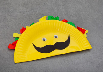 Yellow taco with a mustache on it made out of paper plate
