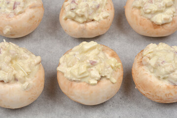 A detailed close-up shows densely arranged stuffed button mushrooms on baking paper, ready for baking