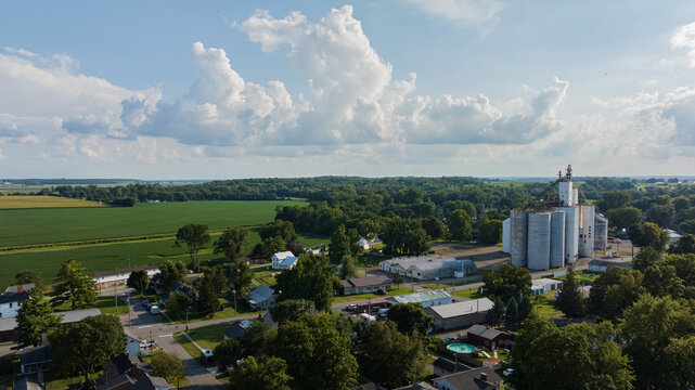 Aerial view of a cluster of silver grain elevators piercing the skyline amidst a tapestry of verdant trees and fields, West Liberty, Ohio, United States.