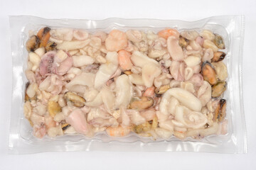 A clear vacuum-sealed package of frozen mixed seafood, including squid, mussels, and shrimp, sits on a white background
