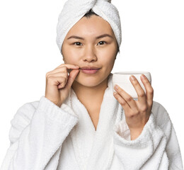 Chinese woman with moisturizer in robe with fingers on lips keeping a secret.