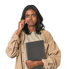 Young Indian woman studying with laptop with fingers on lips keeping a secret.