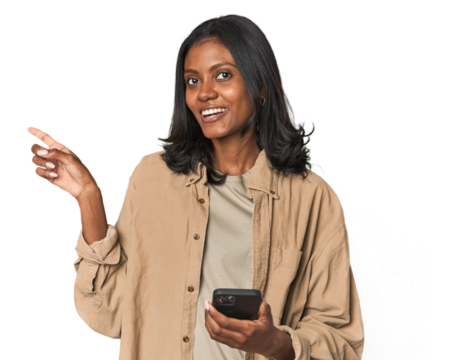 Young Indian woman using a smartphone smiling and pointing aside, showing something at blank space.