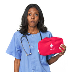 Young Indian nurse with first aid kit shrugs shoulders and open eyes confused.