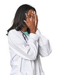 Young Indian doctor with stethoscope blink through fingers frightened and nervous.