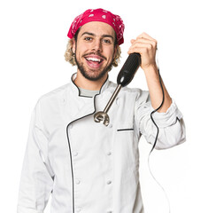 Young Caucasian chef using mixer in studio showing a mobile phone call gesture with fingers.