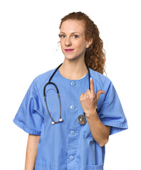 Redhead young caucasian  nurse in studio pointing with finger at you as if inviting come closer.