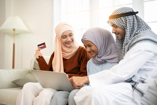 Muslim family shopping online with a credit card on their laptop in living room at home