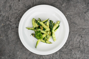 Cucumber salad with garlic in a white plate on a gray concrete background