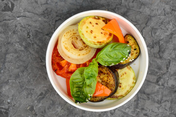Grilled vegetables with basil in a disposable dish on a gray concrete background