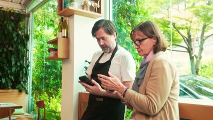 Cafe owner and financial advisor reviewing business data on smart phones inside a cozy coffee shop. Bright natural light and greenery enhance the productive and collaborative workspace atmosphere. - Powered by Adobe