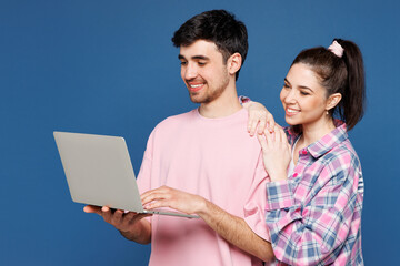 Young smiling couple two friends family IT man woman they wearing pink casual clothes together hold use work on laptop pc computer isolated on plain blue background studio portrait. Lifestyle concept.