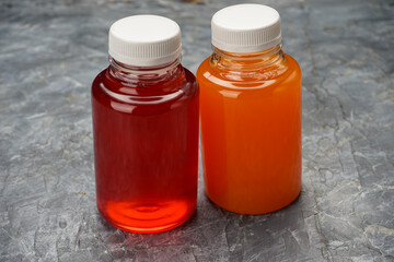 carrot and cherry juice in a transparent bottle on a gray concrete background