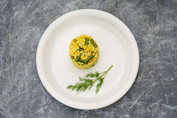 Bulgur with vegetables in a white plate with greens on a gray concrete background