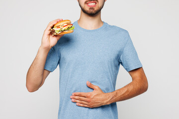 Young man he wearing blue casual clothes hold eat burger put hands on abdomen suffer from stomach...