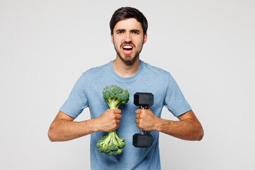 Young strong sporty man wear blue t-shirt casual clothes hold broccoli and dumbbell do sport...
