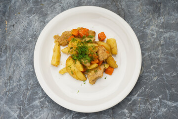 stewed potatoes with vegetables in a white plate on a gray concrete background