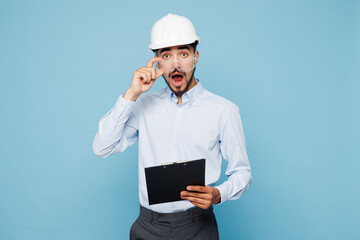 Young shocked architect engineer designer employee man wearing white clothes glasses shirt hardhat...