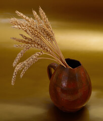Wheat ears in clay jug on golden background
