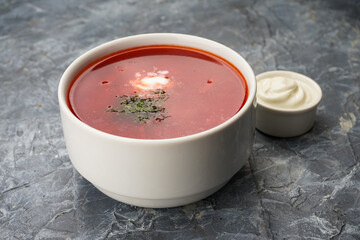 borsch with herbs and sour cream in a white plate on a gray background