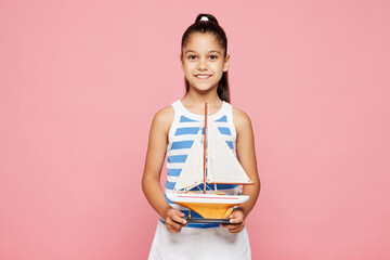 Traveler kid child wears blue casual clothes hold little boat isolated on plain pink background....