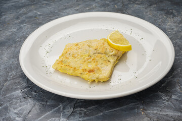 fish fillet with lemon in a white plate on a gray concrete background