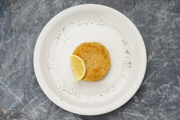 fish cutlet with lemon in a white plate on a gray concrete background